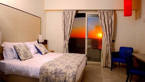 A hotel room with a bed, a desk, and a view of a sunset through the window.
