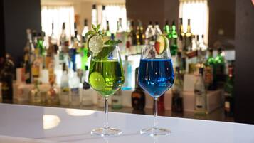 Two cocktails on a bar counter with a background of various bottles.
