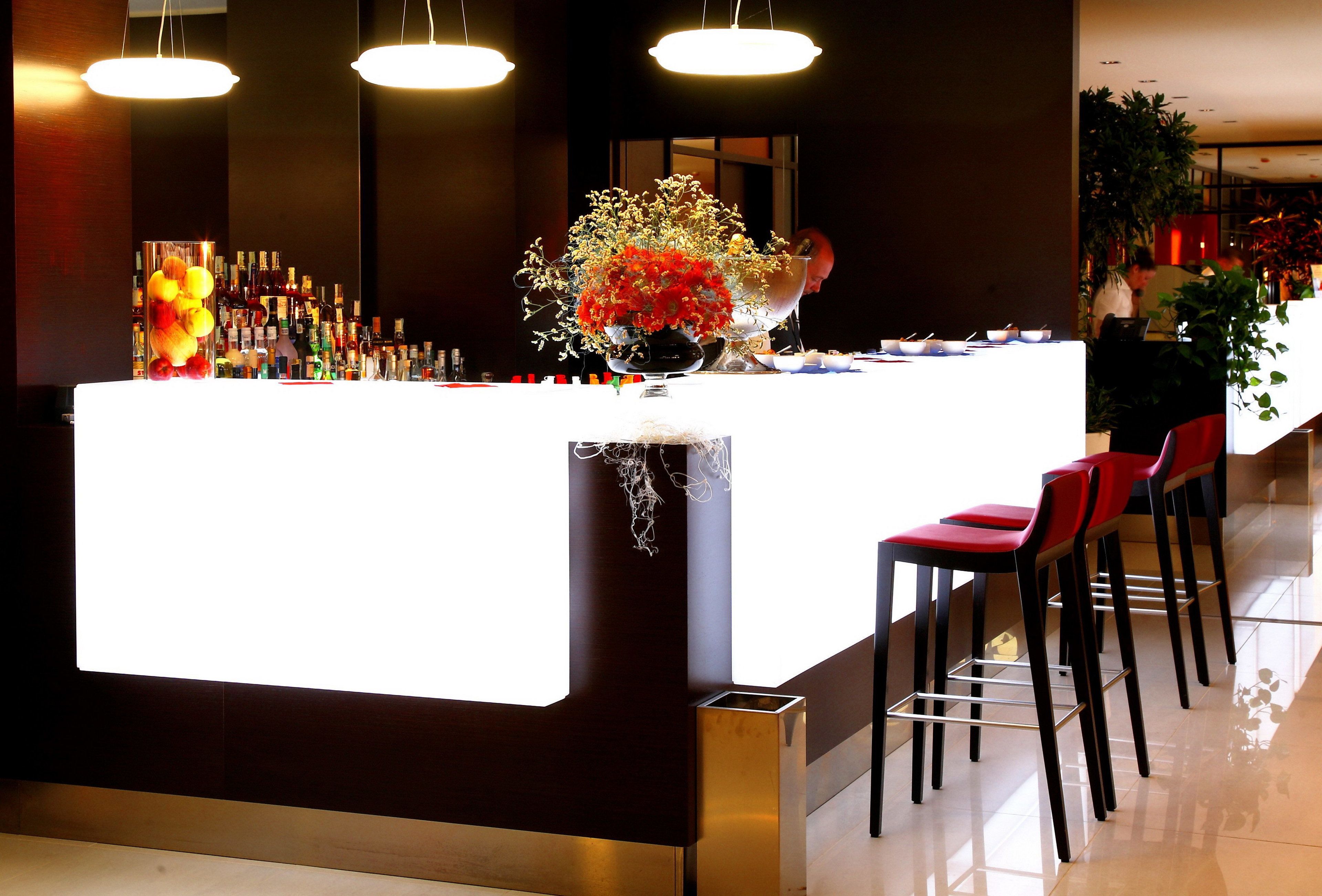 A modern bar area with a white counter, red bar stools, and a variety of bottles.