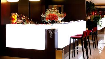A modern bar area with a white counter, red bar stools, and a variety of bottles.