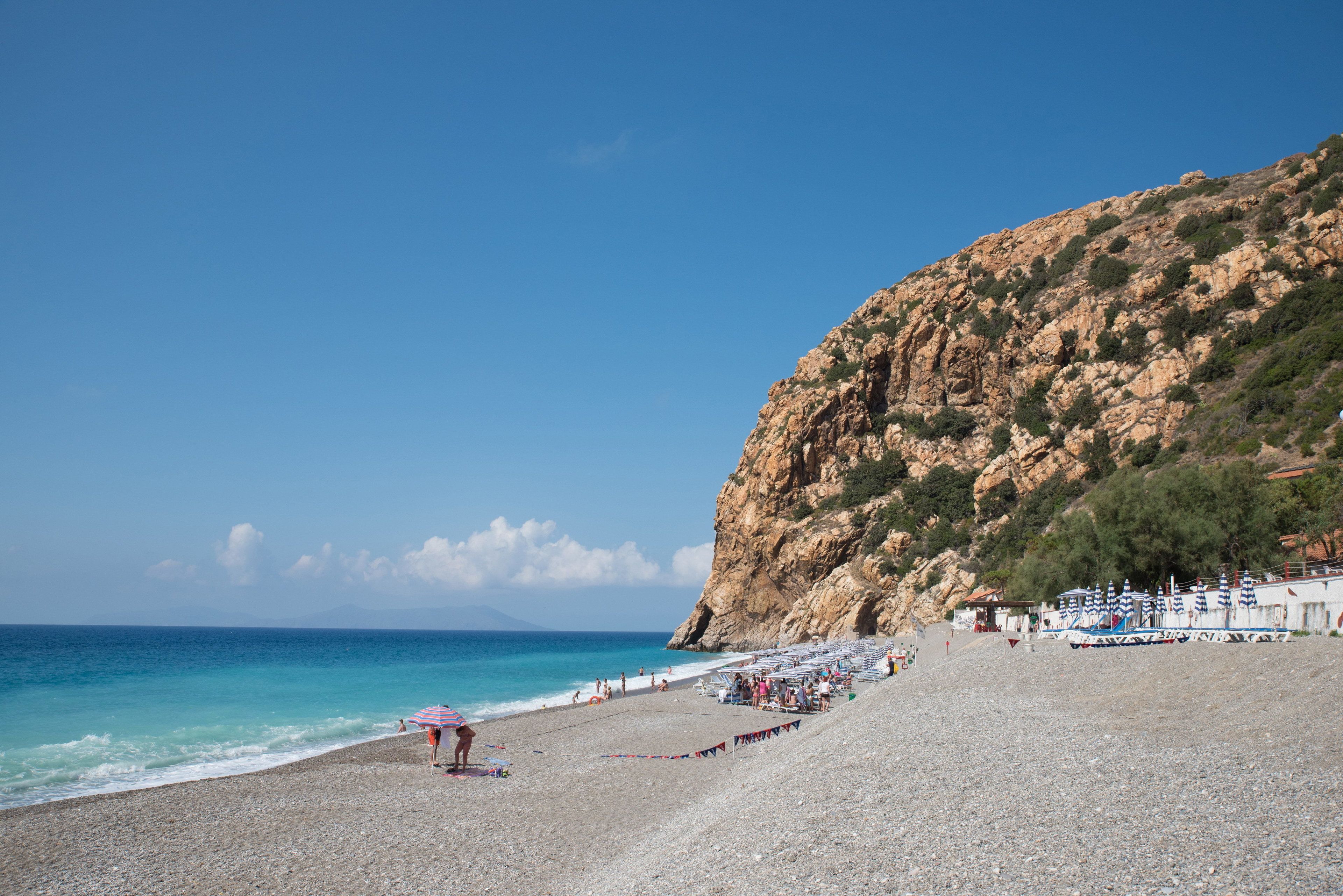 A pebble beach with umbrellas and a rocky cliff.