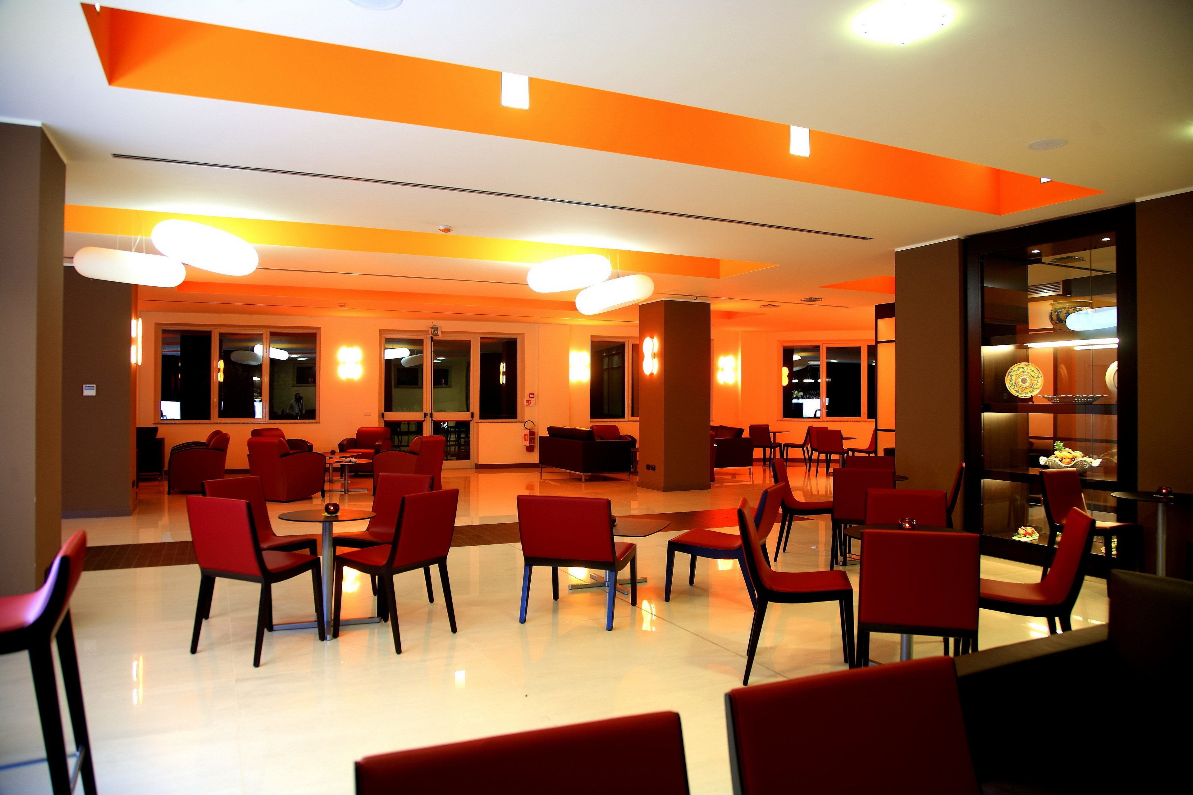 Un comedor moderno con sillas y mesas rojas, iluminado por luces colgantes.