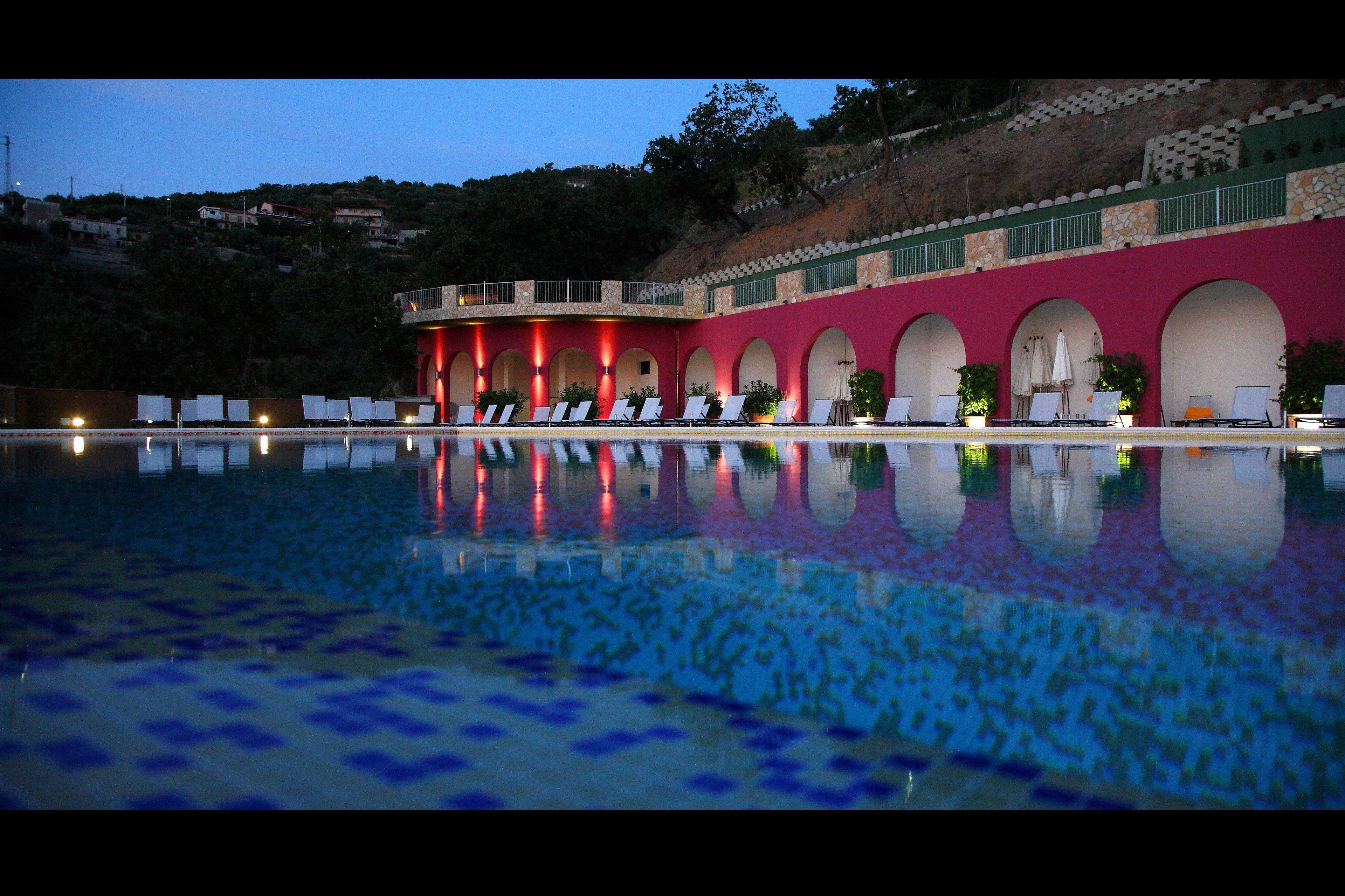 A swimming pool with a reflection of a building with arches and a red facade.