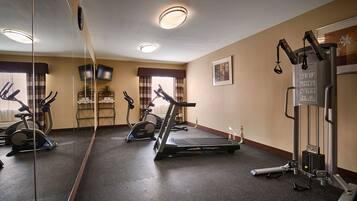 A hotel fitness center with exercise equipment, a mirror, and a wall-mounted TV.
