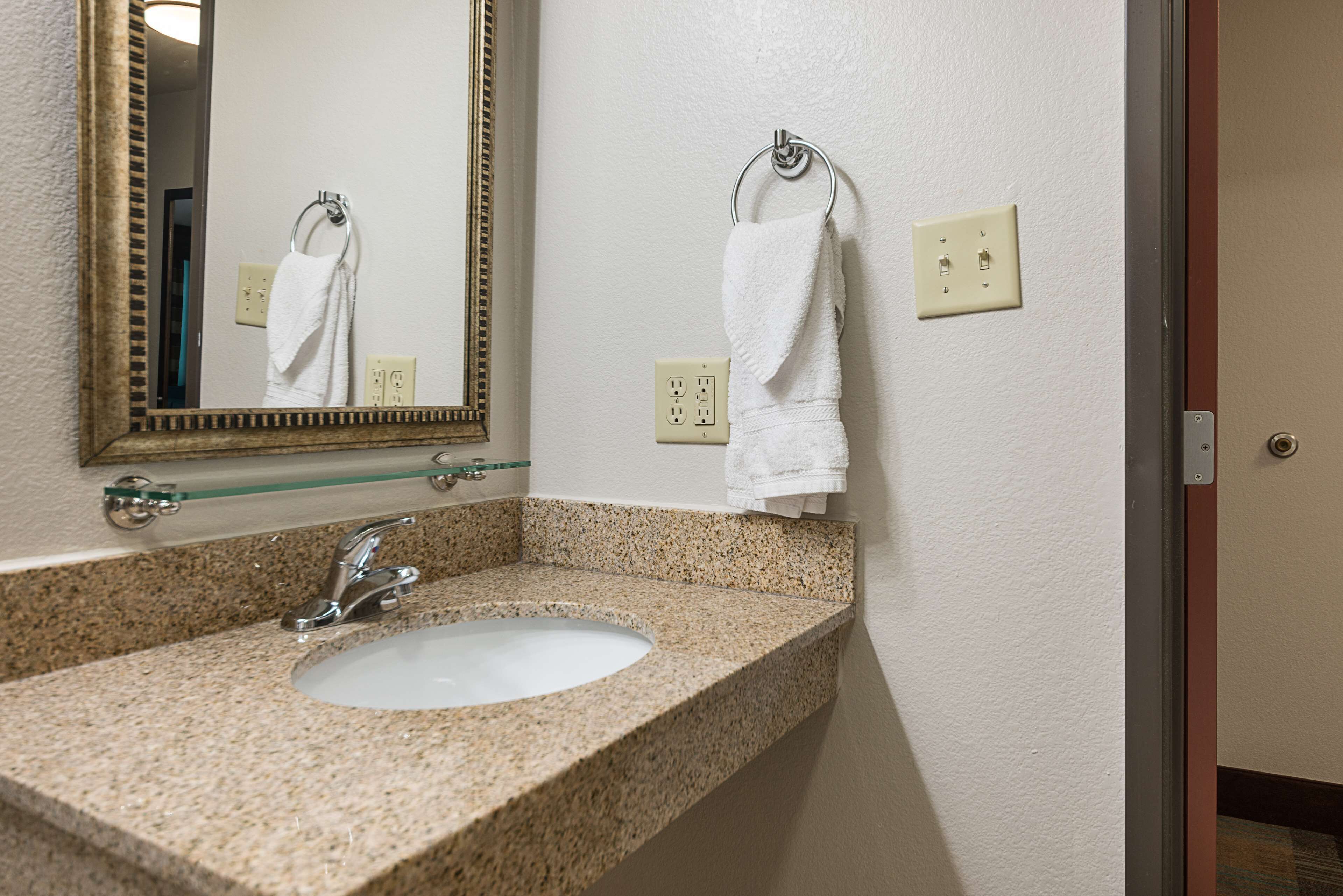 A bathroom with a granite countertop sink, a mirror, and two towels hanging on hooks.
