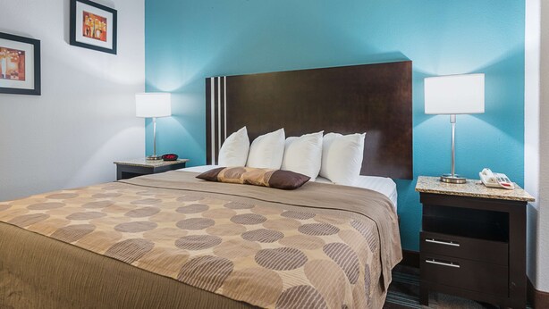 A hotel room with a large bed, two bedside tables with lamps, a headboard, and framed pictures on the wall.