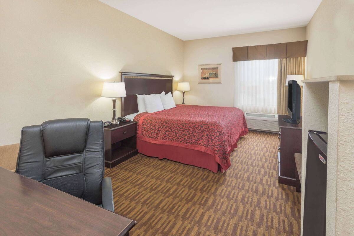 A hotel room with a bed, a desk, a chair, a television, and a window with curtains.
