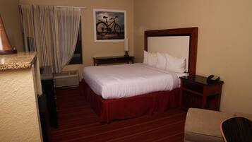 A hotel room with a bed, a desk, a chair, a nightstand, a lamp, and a painting on the wall.