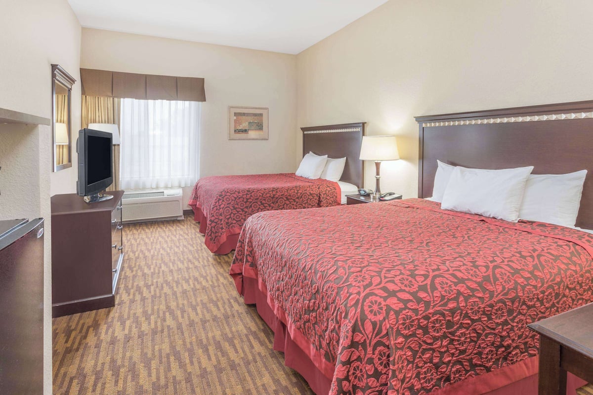 A hotel room with two beds, a TV, a desk, and a window with curtains.