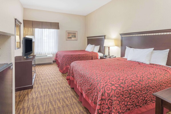 A hotel room with two beds, a TV, a desk, and a window with curtains.