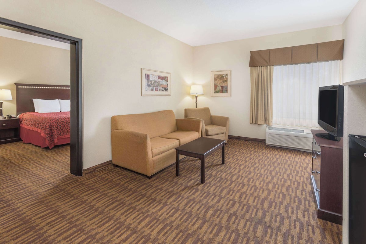A hotel room with a bed, two armchairs, a sofa, a coffee table, a TV, and a desk with a lamp.