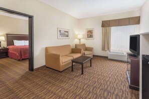 Habitación de hotel con una cama, dos sillones, un sofá, una mesa de centro, un televisor y un escritorio con una lámpara.
