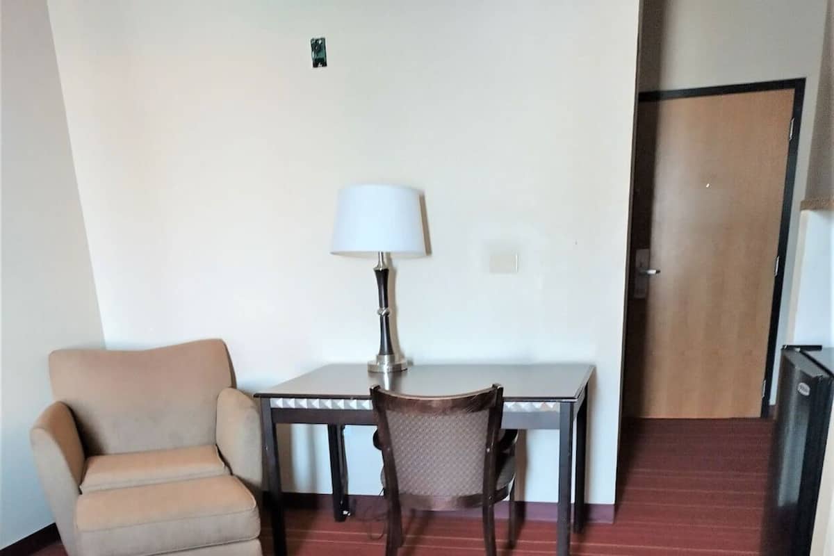 A hotel room with a bed, a desk with a lamp, a chair, and a door.