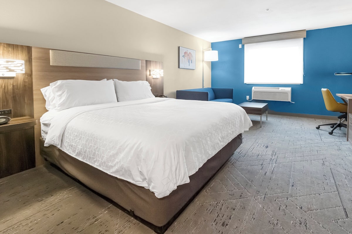 Quarto de hotel com uma cama grande, uma escrivaninha, uma cadeira e uma janela.