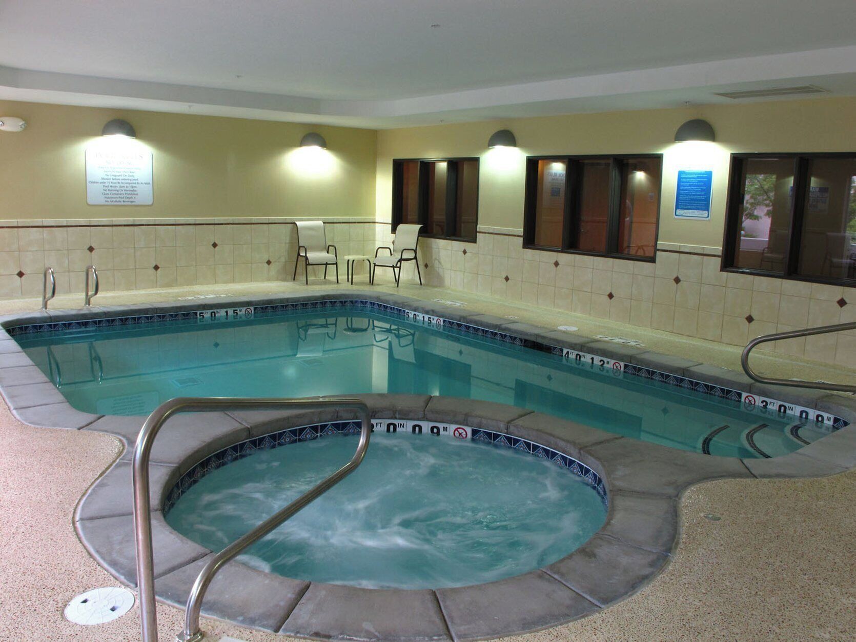 Een binnenzwembad met een jacuzzi, betegelde muren en een zithoek met stoelen.