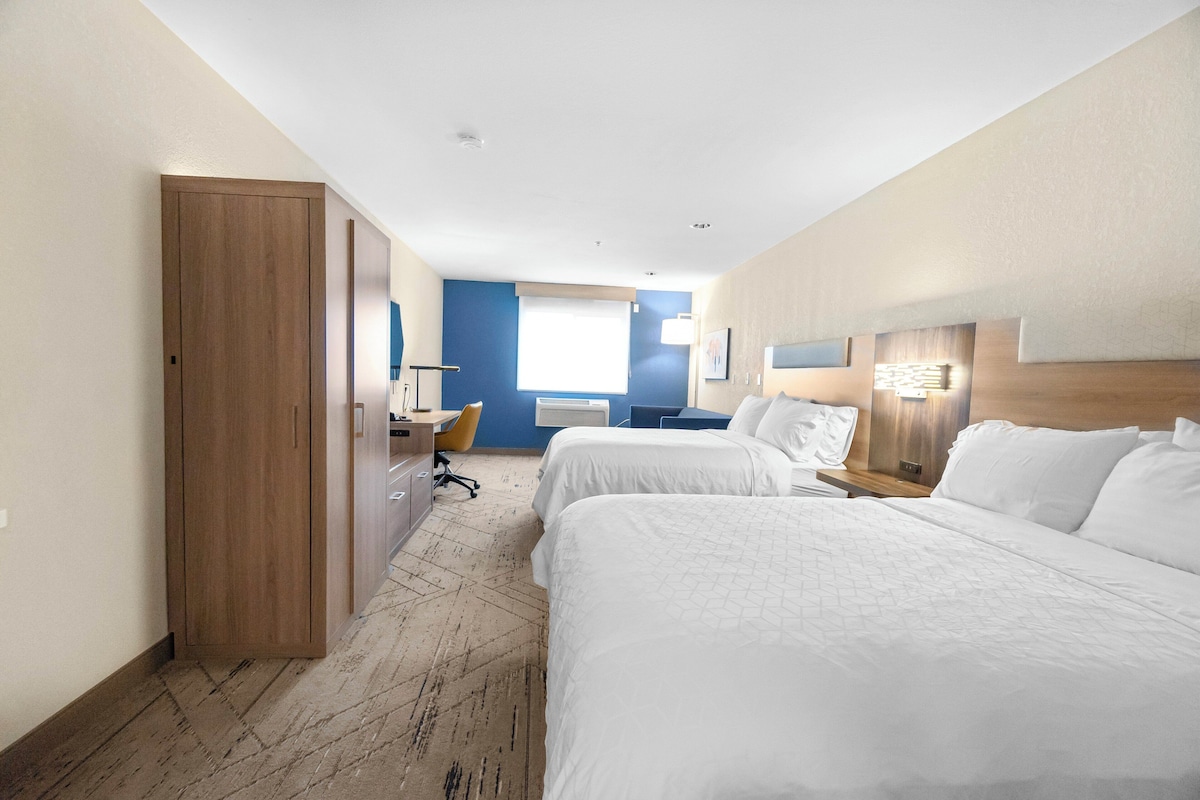 Quarto de hotel com duas camas, uma escrivaninha, uma cadeira e um guarda-roupa.