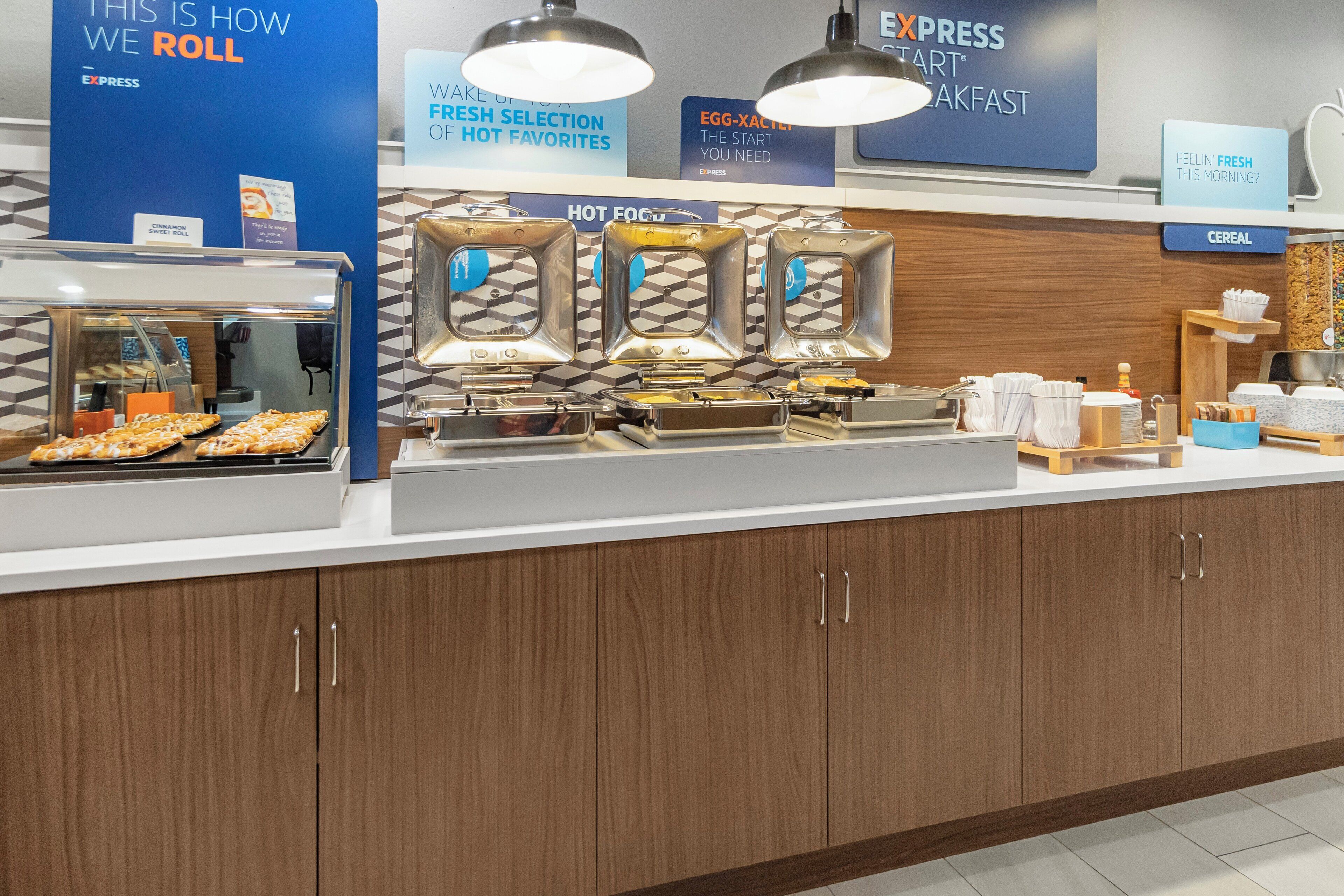 A breakfast station with a display of hot food and cereal options, a sign for Express Start Breakfast, and a sign indicating a selection of fresh favorites.
