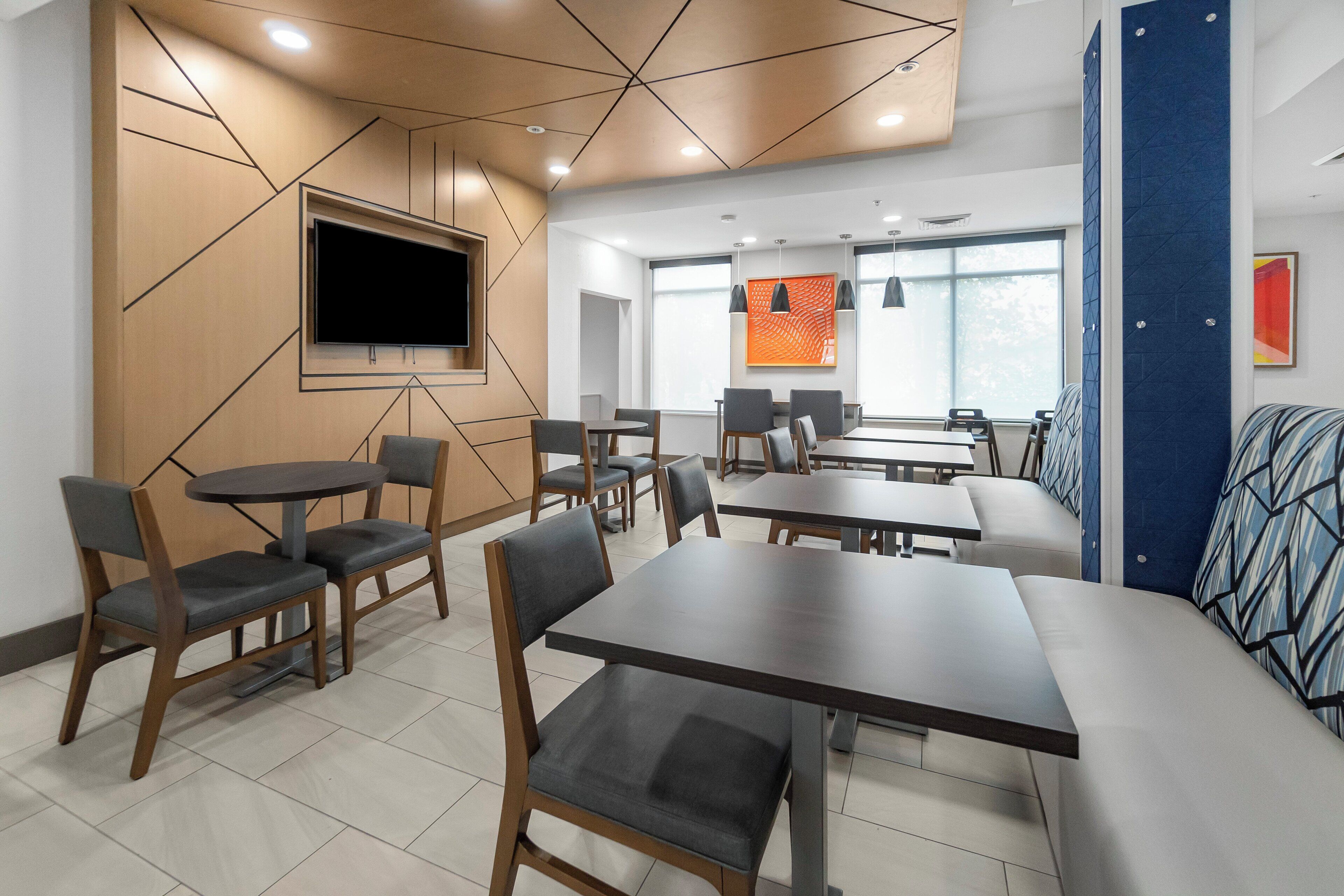 A modern conference room with a large TV, multiple tables and chairs, and a blue accent wall.