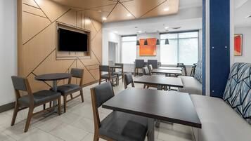 A modern conference room with a large TV, multiple tables and chairs, and a blue accent wall.