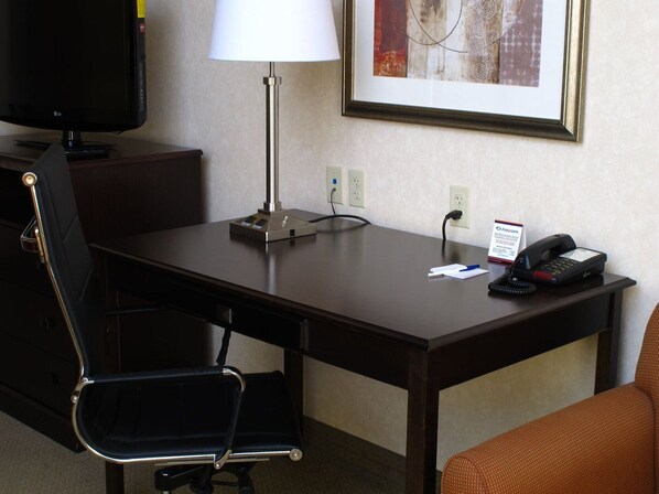 Une chambre d’hôtel équipée d’un bureau, d’une chaise, d’une lampe, d’un téléphone et d’un tableau encadré au mur.