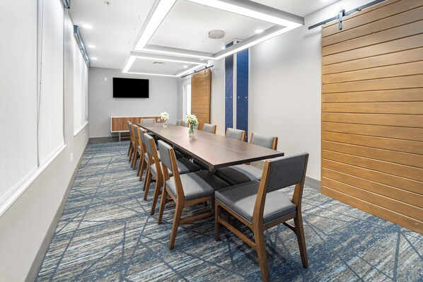 A conference room with a long table, chairs, a flat-screen TV, and a patterned carpet. - Holiday Inn Express Salt Lake City South - Midvale by IHG (Midvale)
