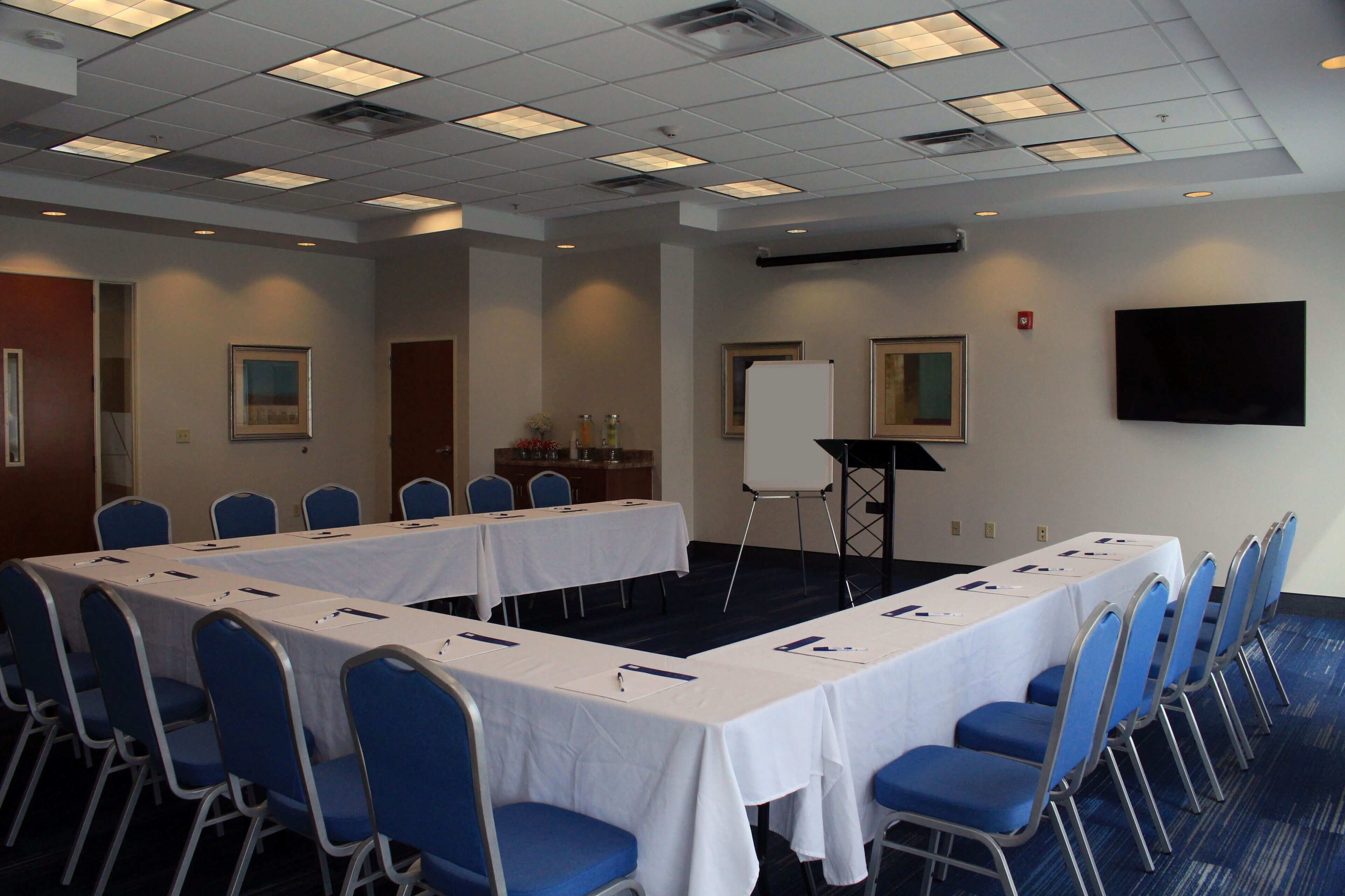 A conference room with a long table, blue chairs, a whiteboard, and a flat-screen TV on the wall.