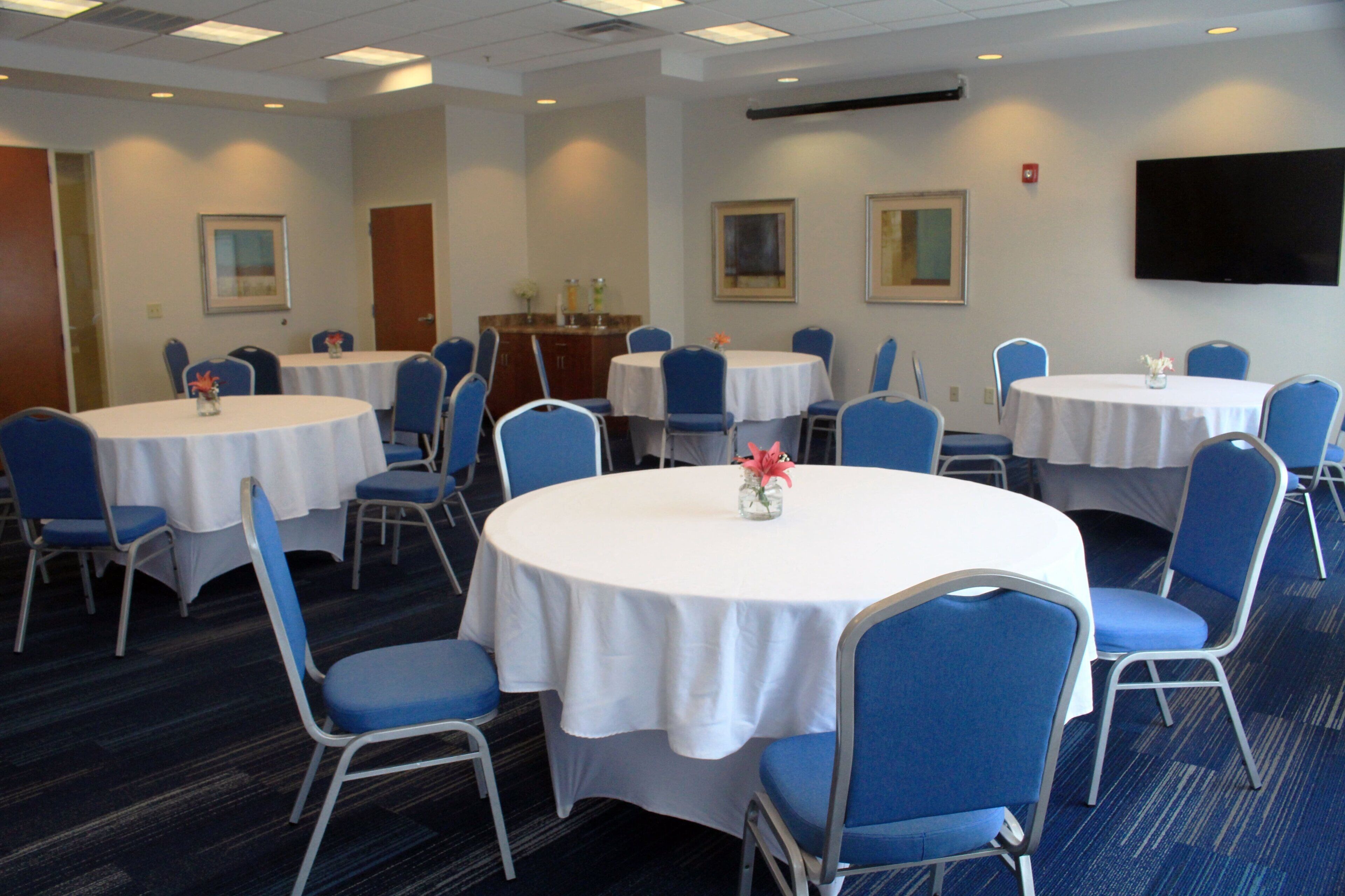 Un salón de conferencias con varias mesas redondas, sillas azules y manteles blancos.