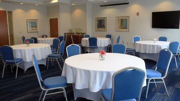 Un salón de conferencias con varias mesas redondas, sillas azules y manteles blancos.