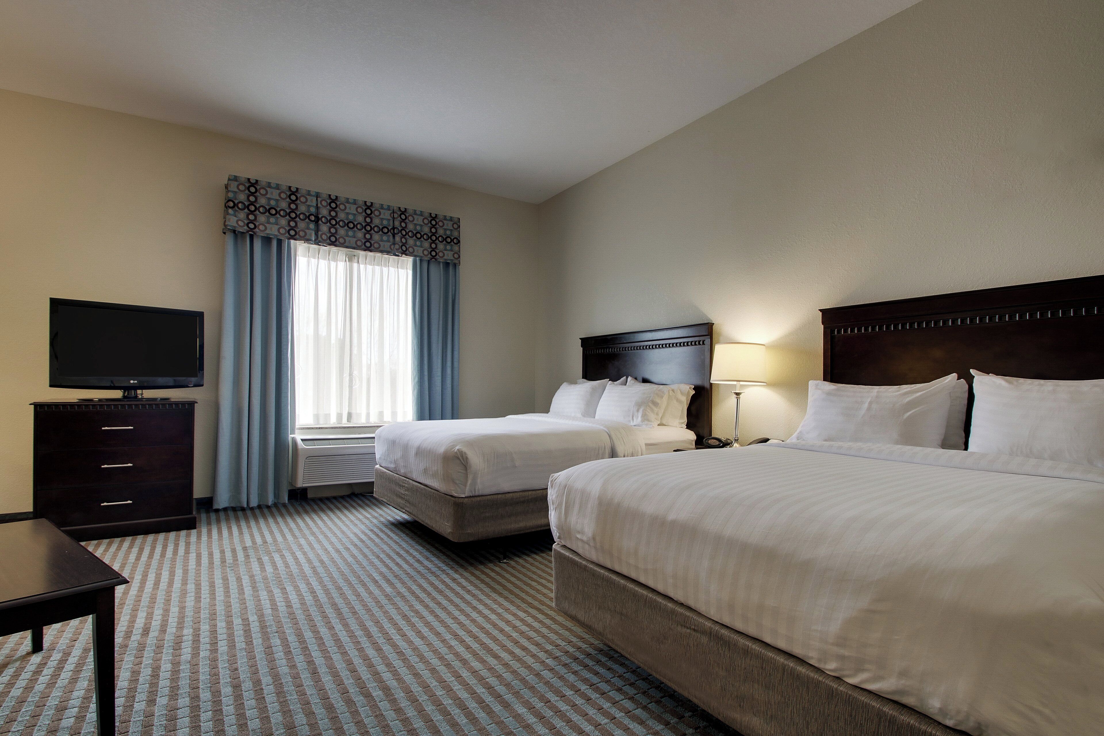 A hotel room with two beds, a TV, a desk, and a window with curtains.