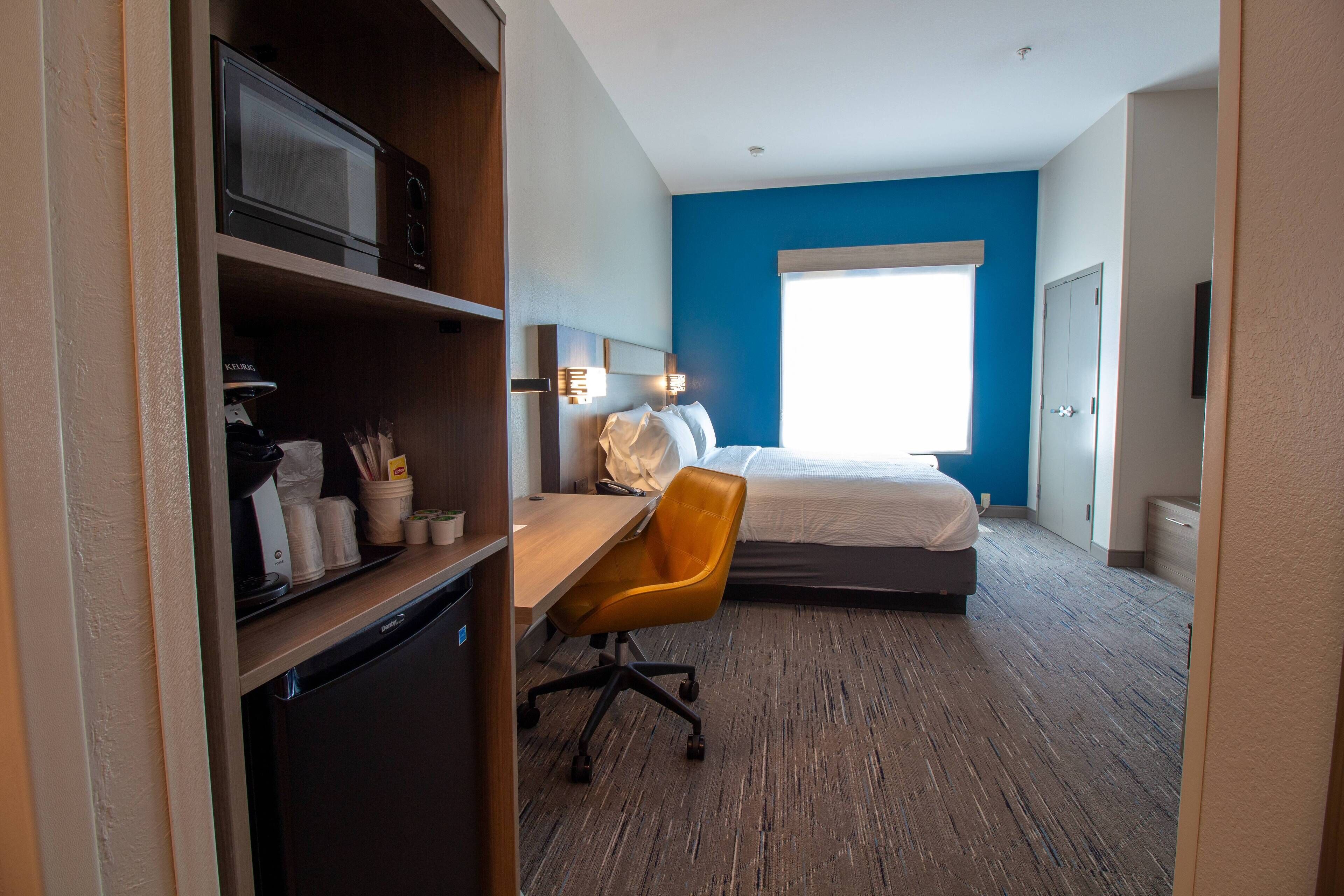Une chambre d’hôtel équipée d’un lit, d’un bureau avec une chaise, d’un four à micro-ondes et d’un petit réfrigérateur.