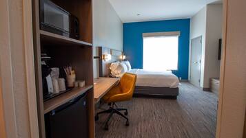 Une chambre d’hôtel équipée d’un lit, d’un bureau avec une chaise, d’un four à micro-ondes et d’un petit réfrigérateur.