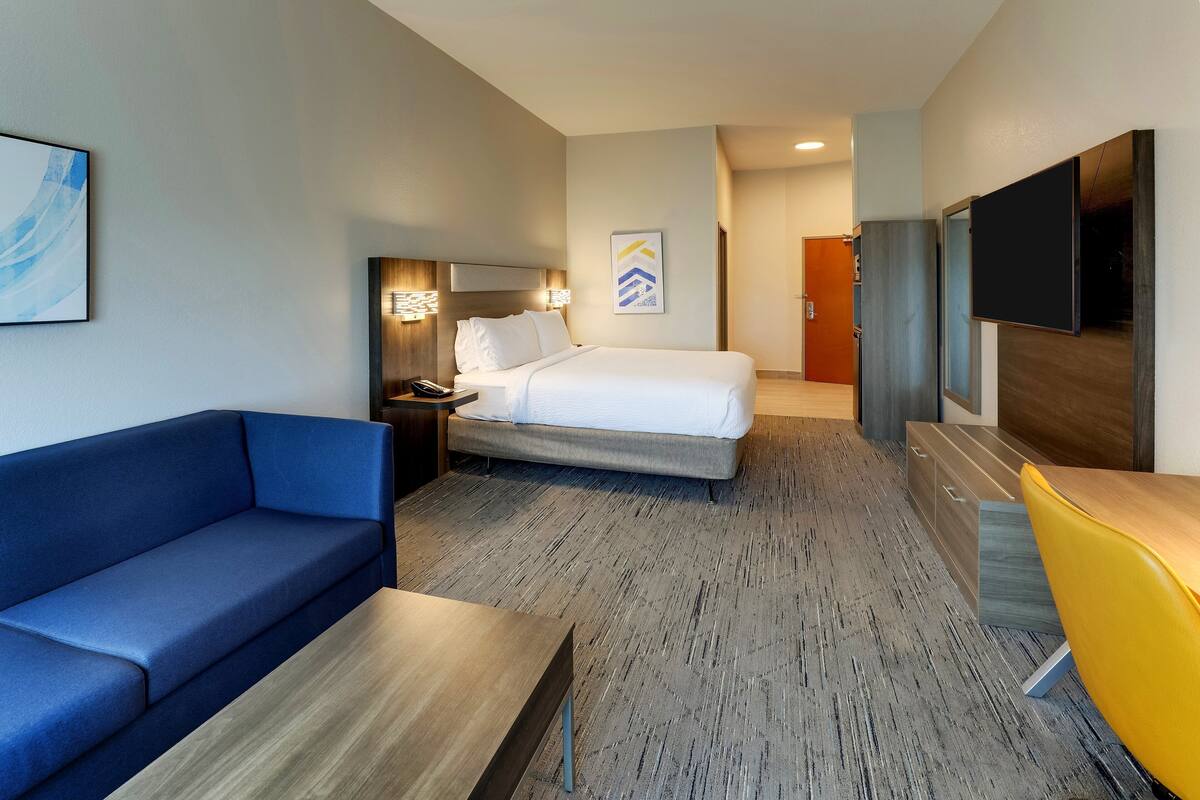 A hotel room with a bed, a blue sofa, a wooden table, a TV, and a desk with a chair.