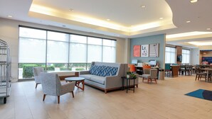 A spacious hotel lobby with a large seating area, a reception desk, and a view of the outdoors. - Holiday Inn Express Leland - Wilmington Area by IHG (Leland)