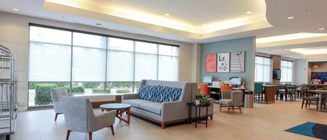 A spacious hotel lobby with a large seating area, a reception desk, and a view of the outdoors.