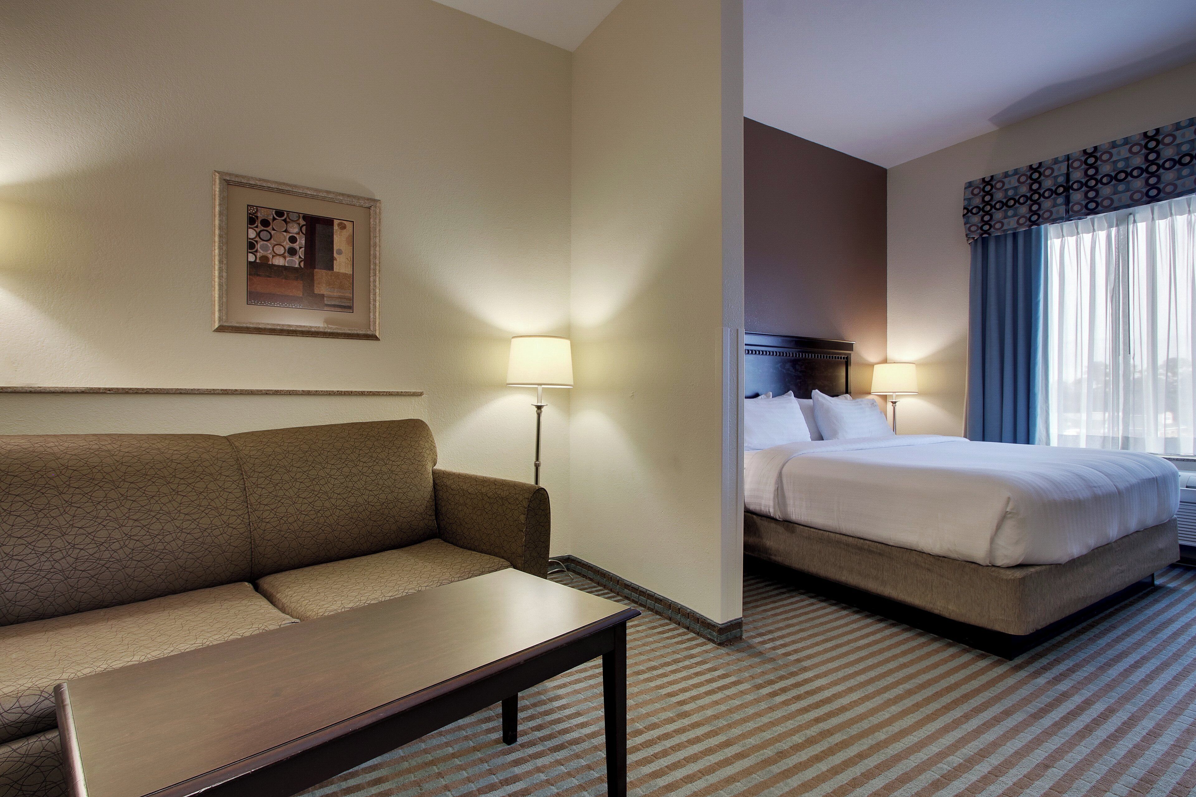 A hotel room with a sofa, a small table, a bed, and two bedside lamps.