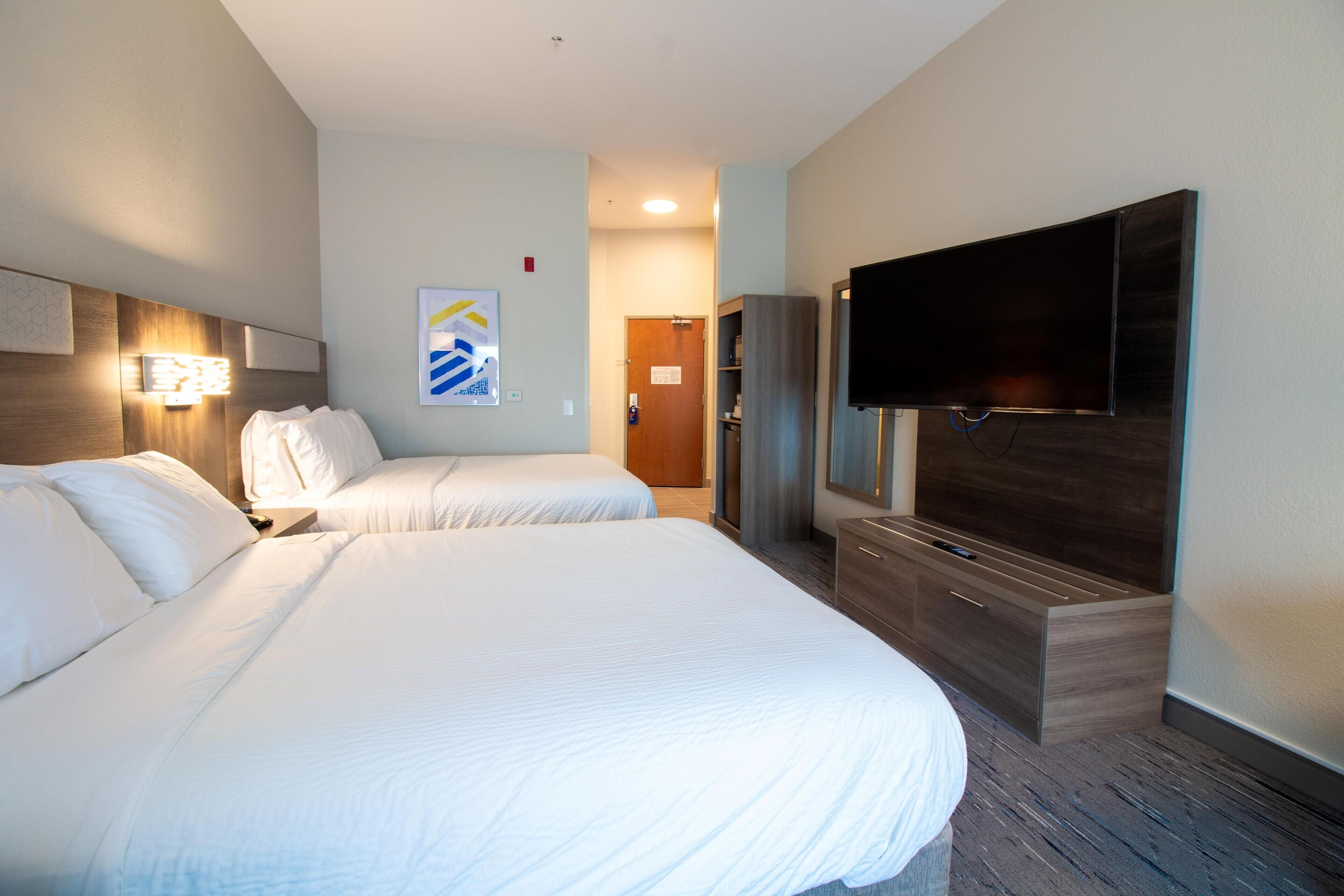 Ein Hotelzimmer mit zwei Betten, einem Flachbildfernseher, einem Holzschrank und einem Wandbild.