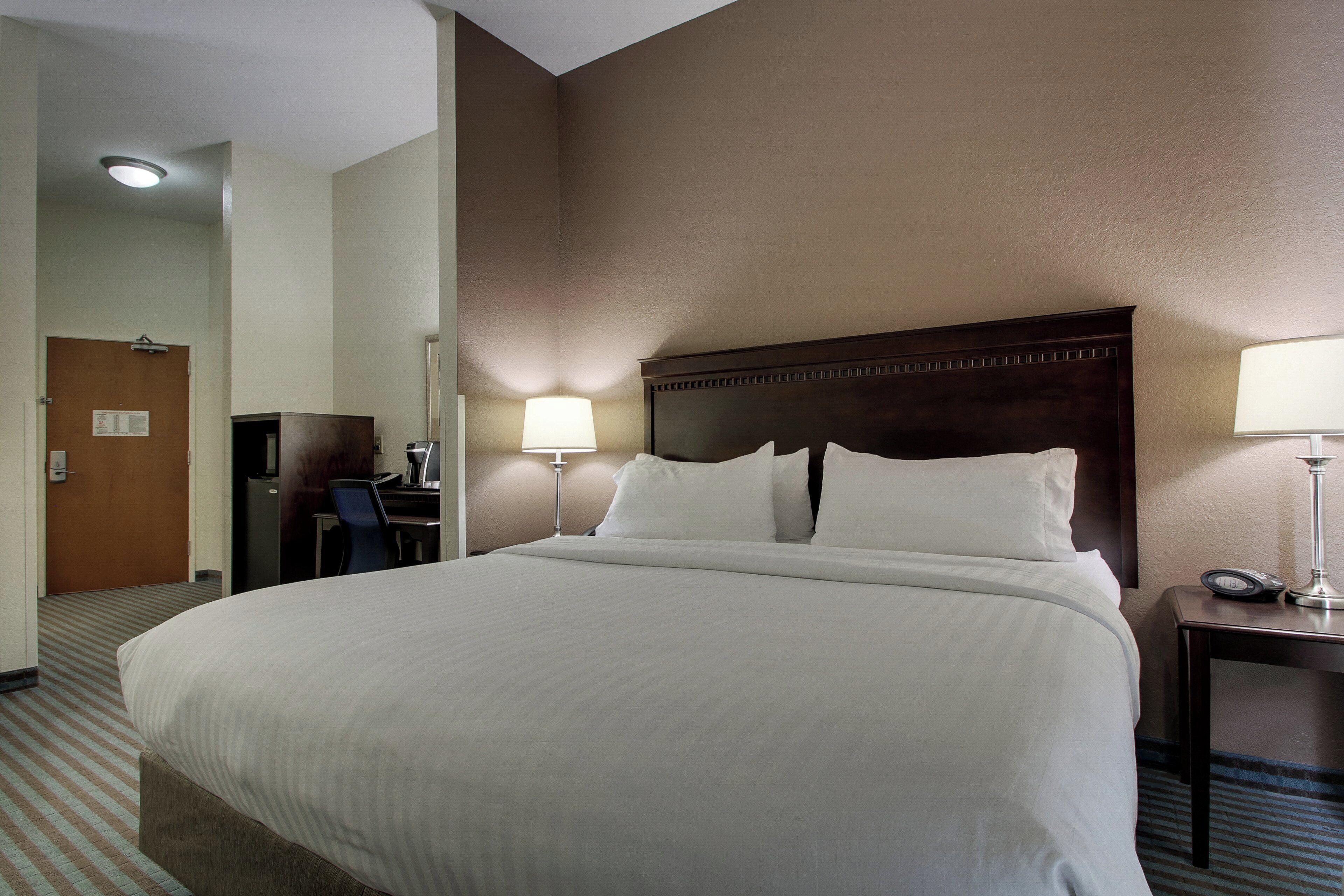 A hotel room with a large bed, a desk with a chair, a lamp, and a clock on the bedside table.