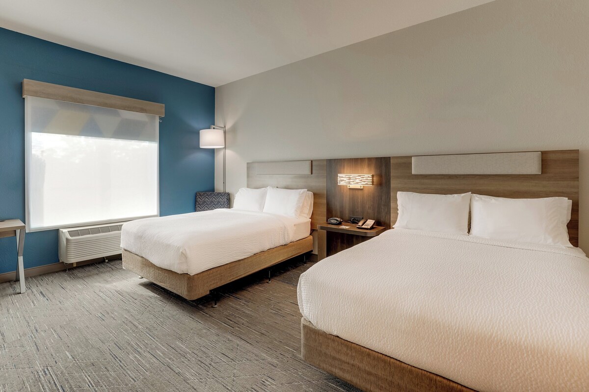 Een hotelkamer met twee bedden, een bureau en een raam met zonwering.