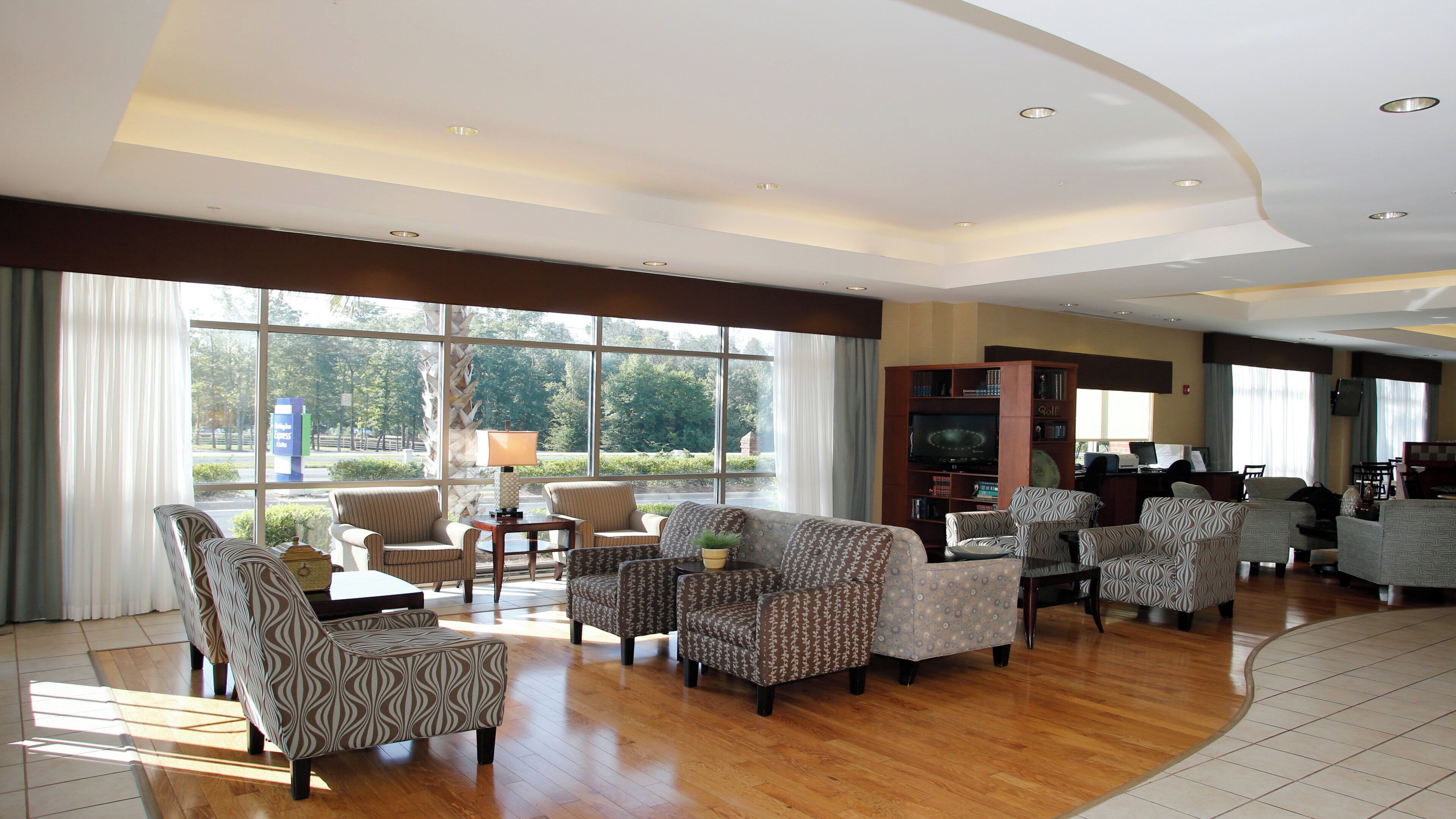 A spacious hotel lobby with multiple seating areas, a television, and a view of the outdoors.