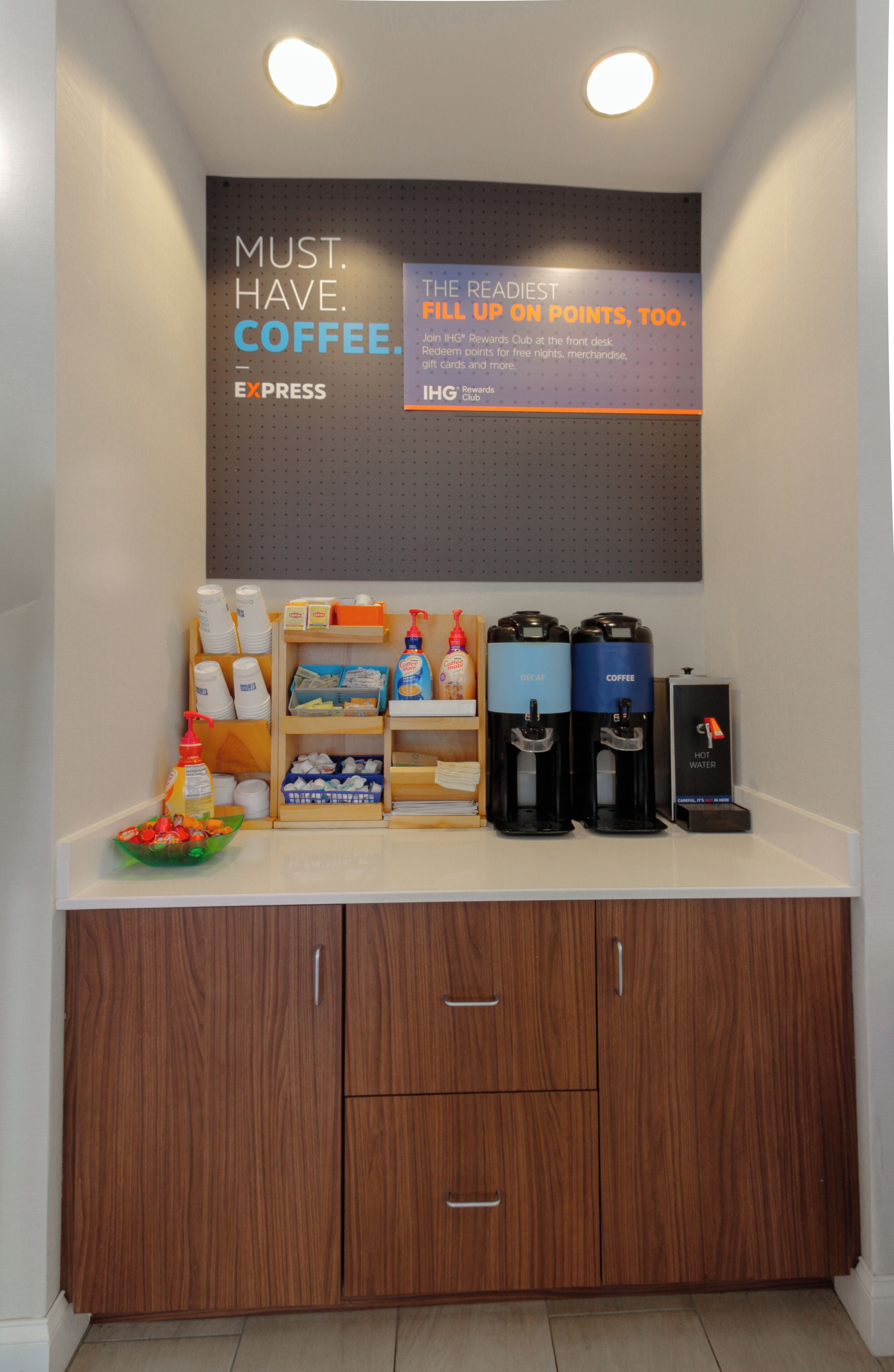 A coffee station with branded dispensers, a promotional sign, and a neatly organized counter.