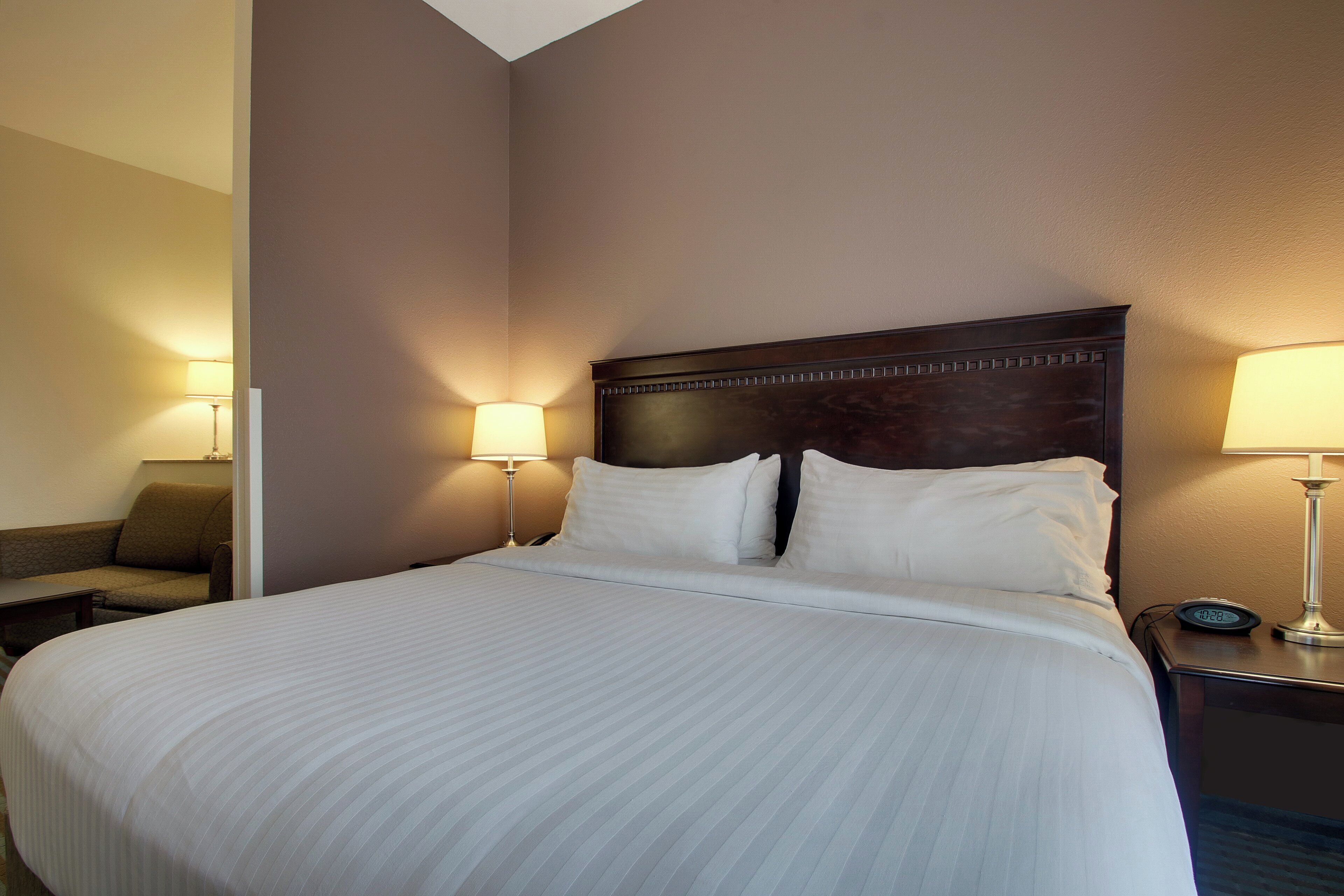 A hotel room with a large bed, two bedside lamps, a nightstand, and a chair.
