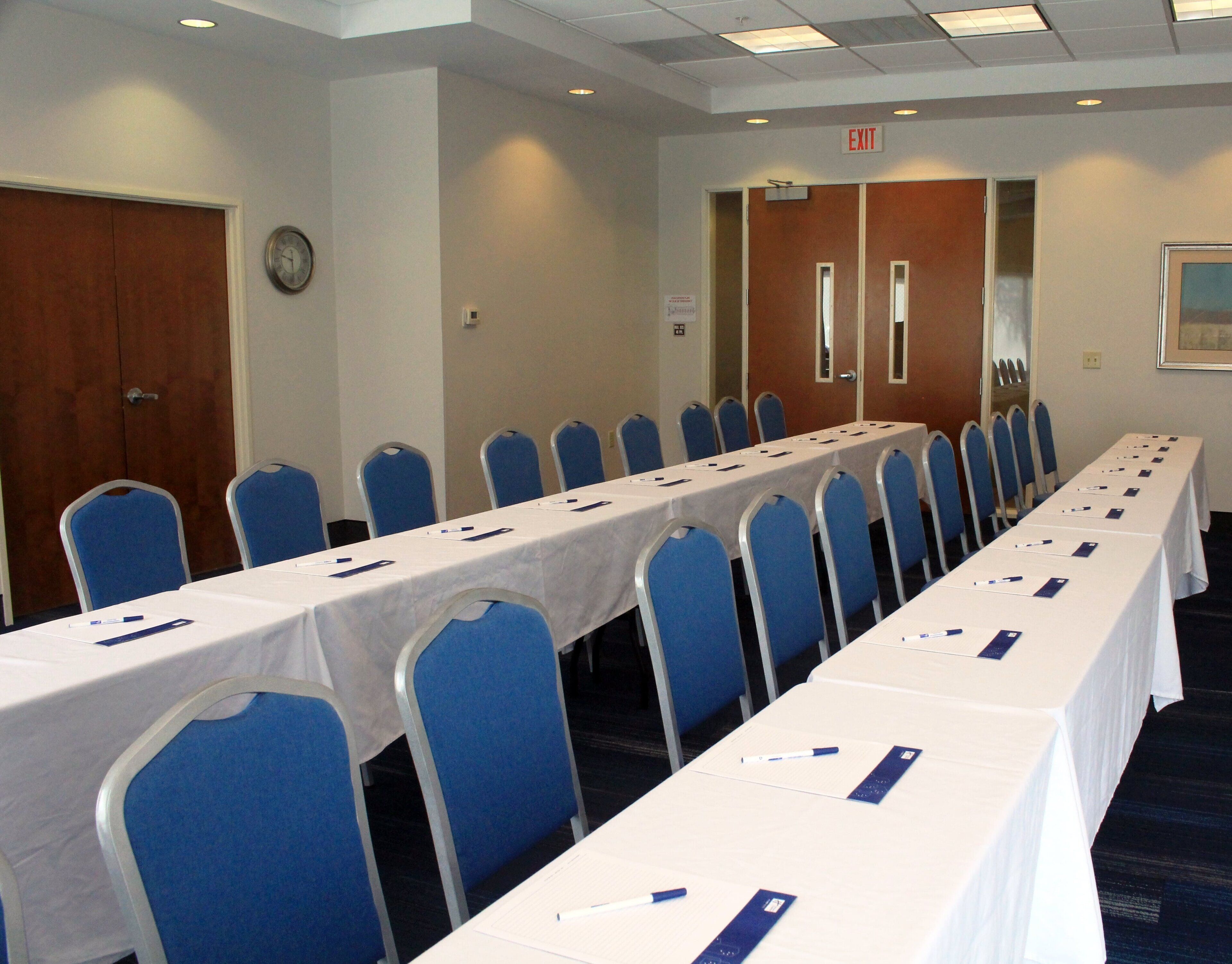 A conference room with a long table, blue chairs, and an exit sign on the wall.