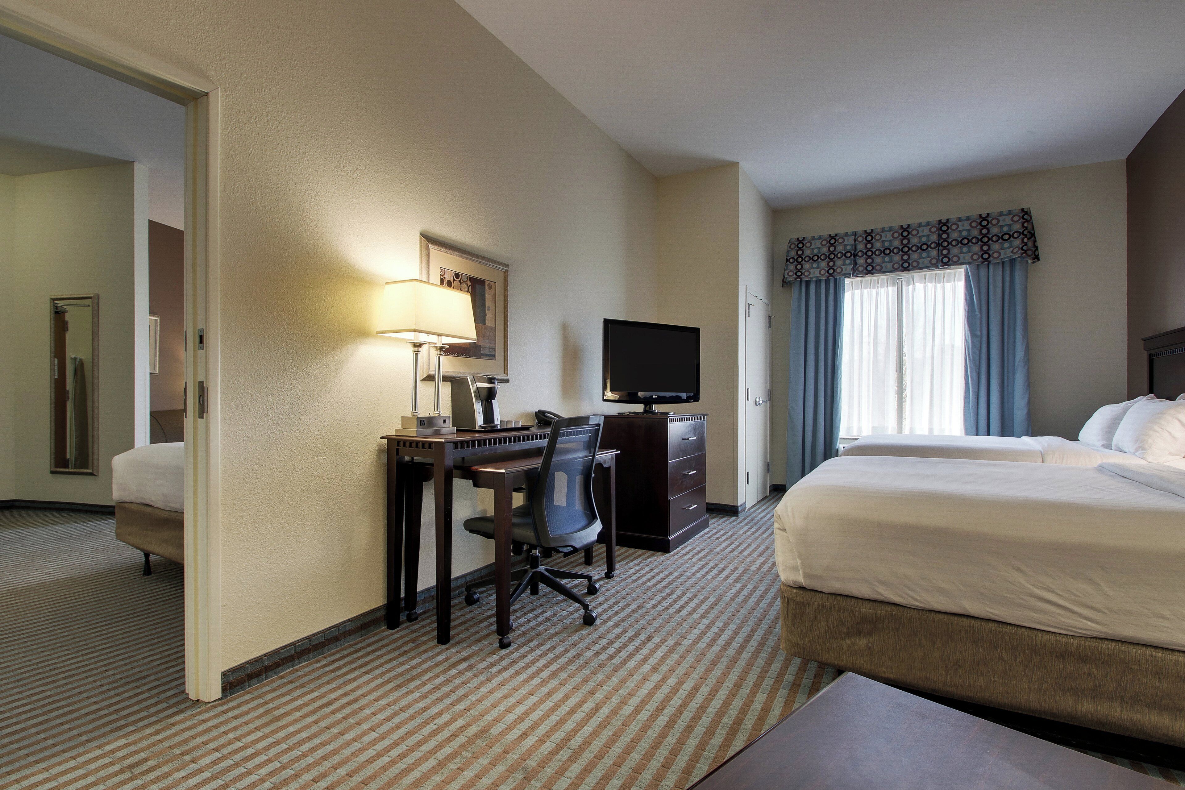 A hotel room with a bed, a desk with a chair, a television, and a window with curtains.