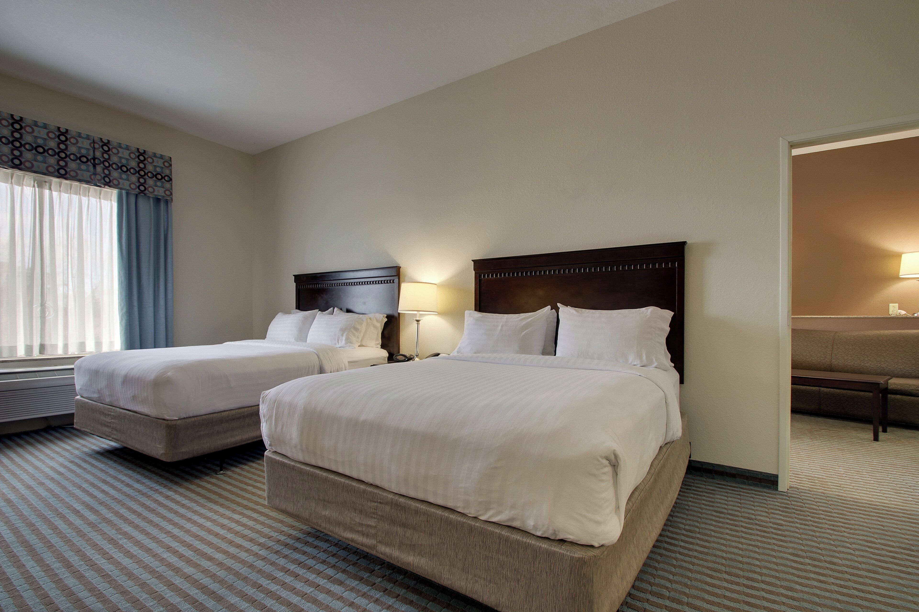Une chambre d’hôtel avec deux lits, une table de chevet avec une lampe, une fenêtre avec des rideaux et une vue sur l’extérieur.
