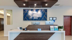 A hotel reception desk with a modern design, featuring a wooden accent and a blue geometric wall art piece above. - Holiday Inn Express Leland - Wilmington Area by IHG (Leland)