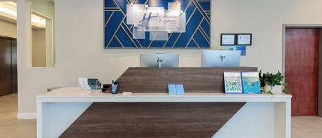 A hotel reception desk with a modern design, featuring a wooden accent and a blue geometric wall art piece above.