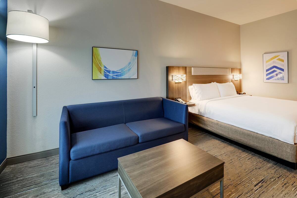 A hotel room with a bed, a sofa, a small table, and two wall-mounted lamps.