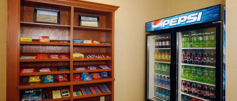 A vending machine stocked with various beverages and snacks, and a wooden shelf unit with packaged food items.