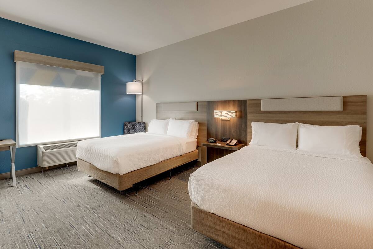 A hotel room with two beds, a desk, and a window with blinds.