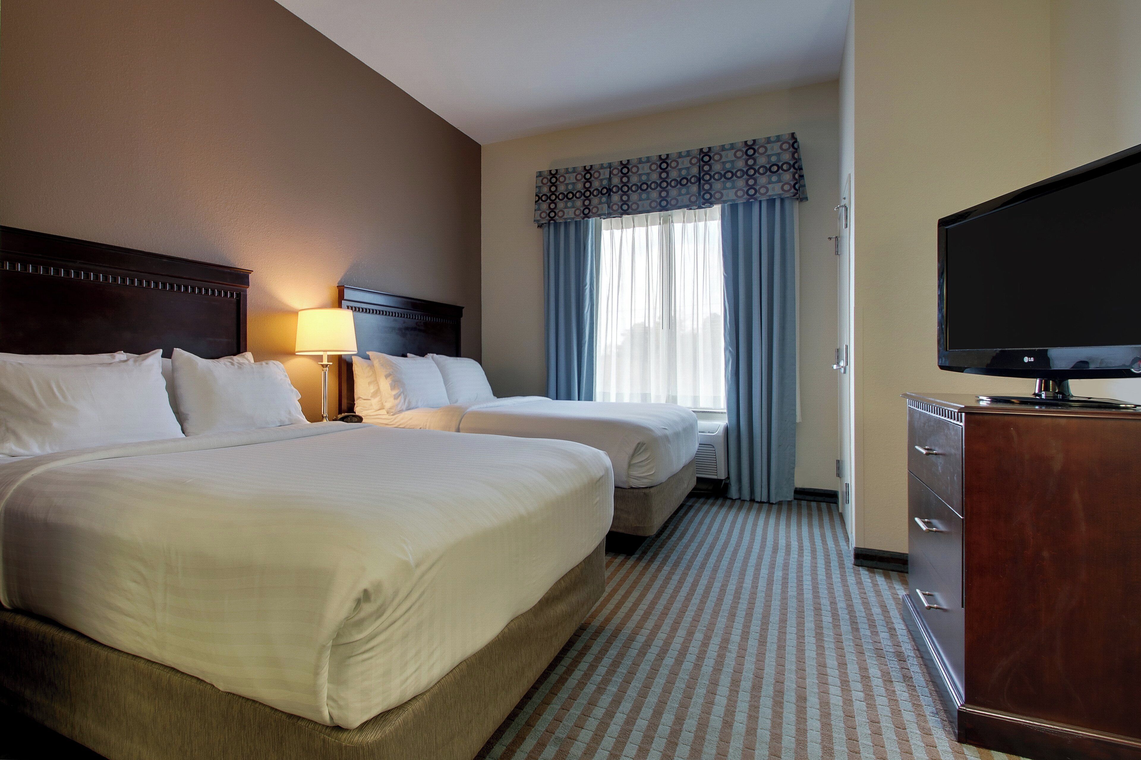 A hotel room with two beds, a TV, a dresser, and a window with curtains.